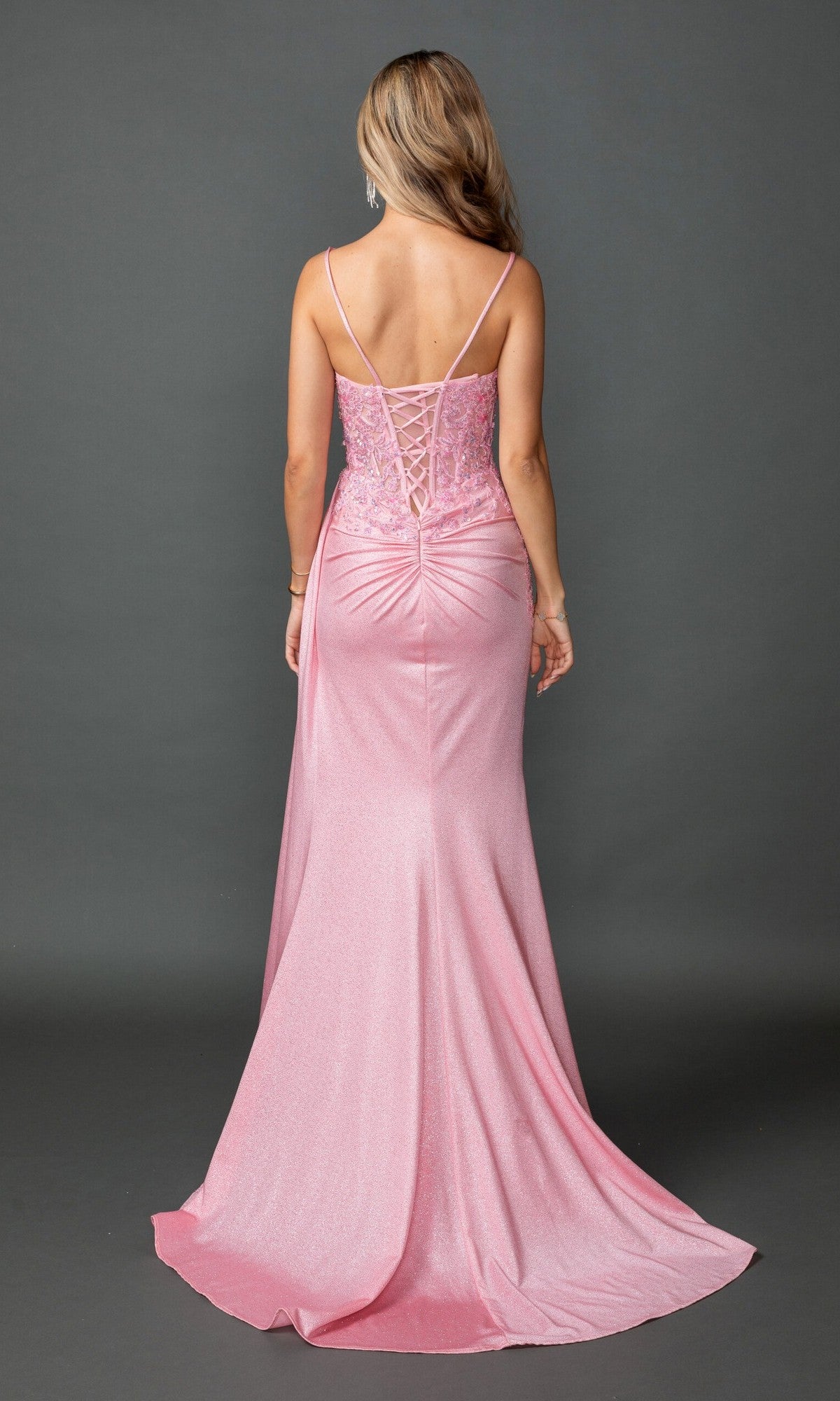 A woman faces away in the Beaded-Bodice Pink Prom Gown: Dancing Queen 4556, a shimmery pink dress with a corset-style bodice, thin straps, and lace-up back against a plain gray background.